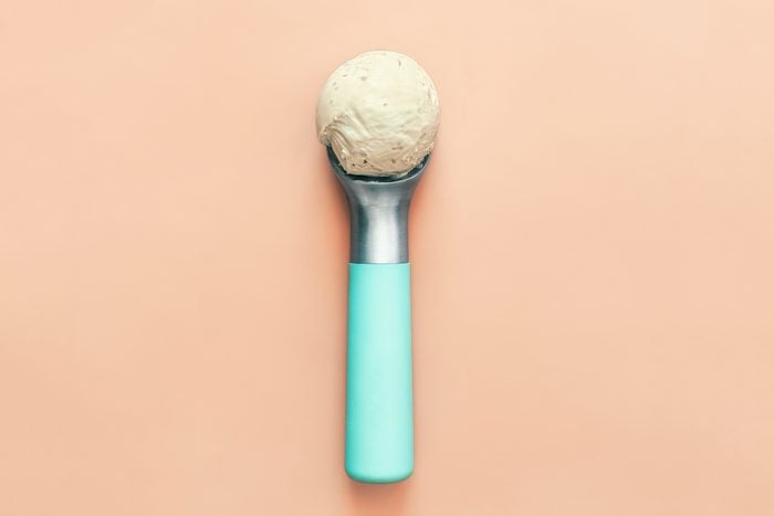 ice cream scoop with one scoop of vanilla ice cream on a light peach colored background