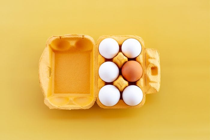 Five white eggs and one brown on a yellow background
