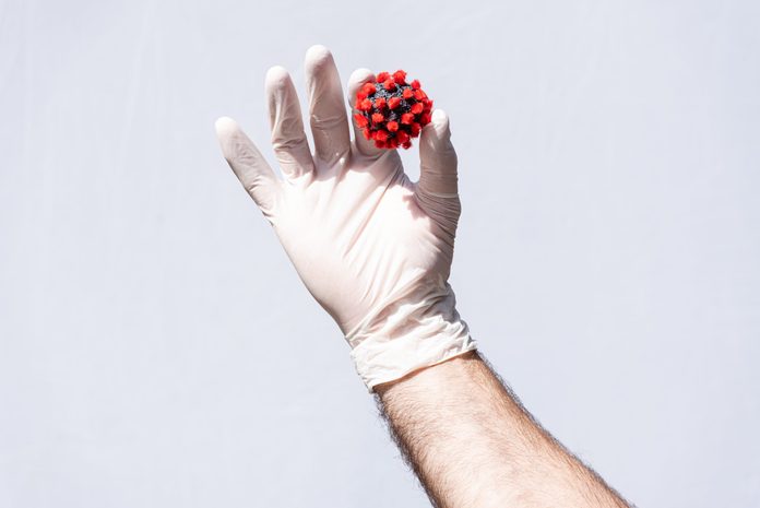 Man's hand wearing a white protective glove, holding a coronavirus model