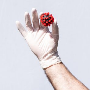 Man's hand wearing a white protective glove, holding a coronavirus model