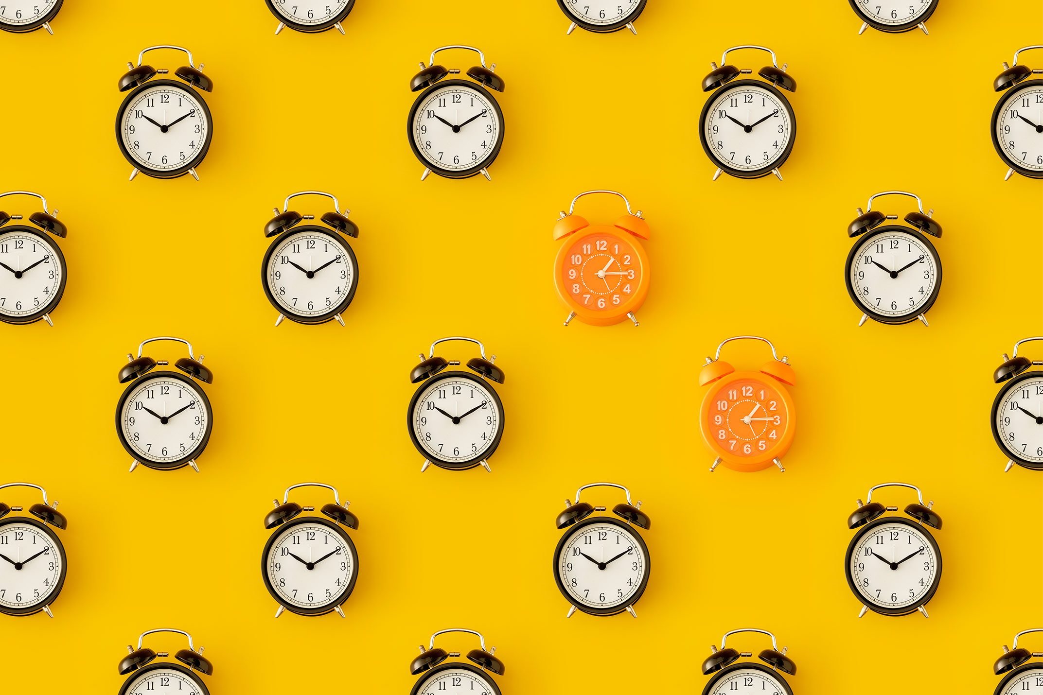 pattern of clocks on a yellow background; all clocks are black alarm clock except two that are orange