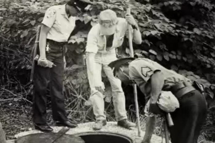 Black and white photo of officers investigating a hole