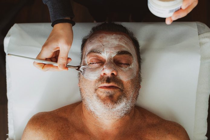 Cropped Hands Applying Cream On Man Face At Spa