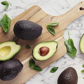 Wooden cutting board with avocados and basil on marble stone