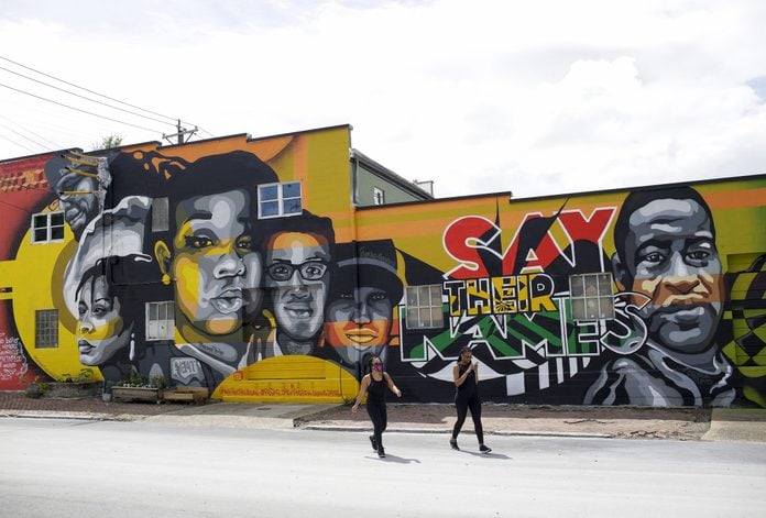 Kimberly King and Genevieve Bell walk away from a mural displaying the face of Breonna Taylor, David McAtee, Sandra Bland, George Floyd and others on a building along 11th Street Saturday, August 1, 2020 in Louisville, Kentucky.