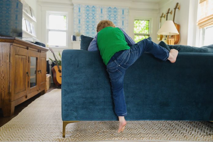 Rear view of boy (4-5) climbing over back of couch
