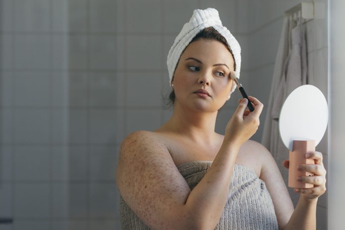 Beautiful Plus Size Woman, Wrapped in a Towel, Applying Makeup onto her Face in the Morning