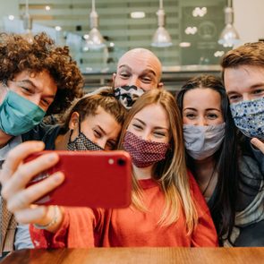 group of friends wearing face masks leaning in together for a selfie in a restaurant