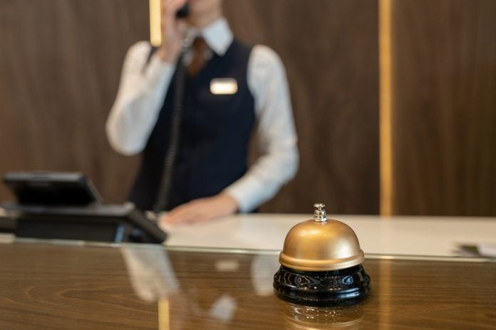 Bell on wooden reception counter against female receptionist consulting clients on the phone