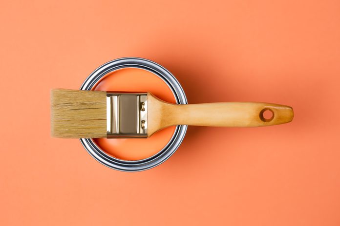 Clean paintbrush on metal bucket with bright orange paint for renovation works on orange coral peach background. Flat lay style. Copy space for your design. Concept of redecoration in home interior. Color swatch for design ideas