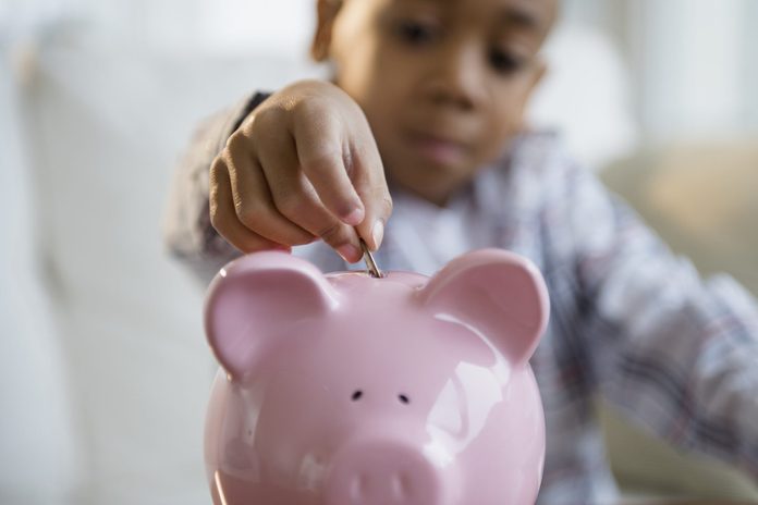 African American boy putting coins in piggy bank
