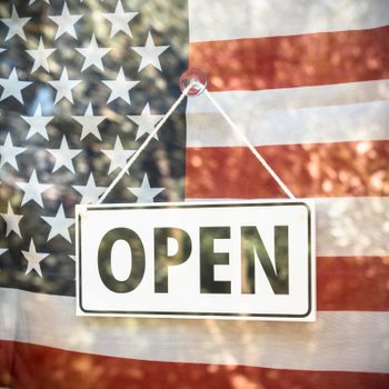 open sign in a store window with american flag behind it