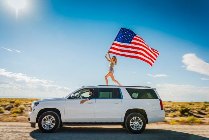 Hispanic woman waving American flag on roof of white SUV