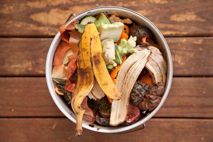 Fruit and vegetable scraps in a small composter on a wood surface background