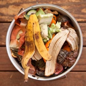 Fruit and vegetable scraps in a small composter on a wood surface background
