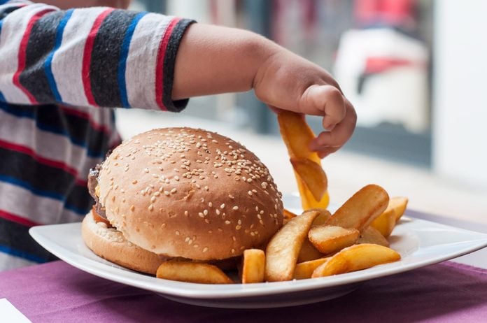 little boy hand eating hamburger and french fries at restaurant