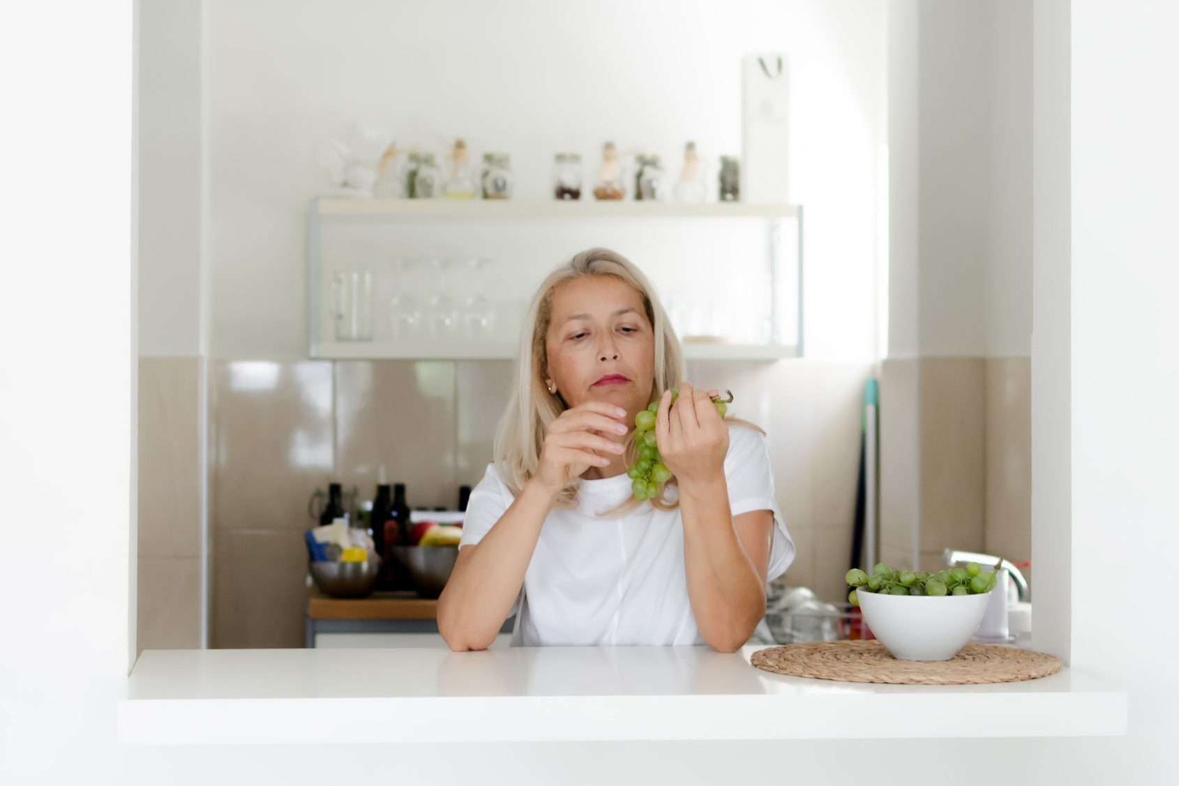 Woman standing in kitchen and eating grapes