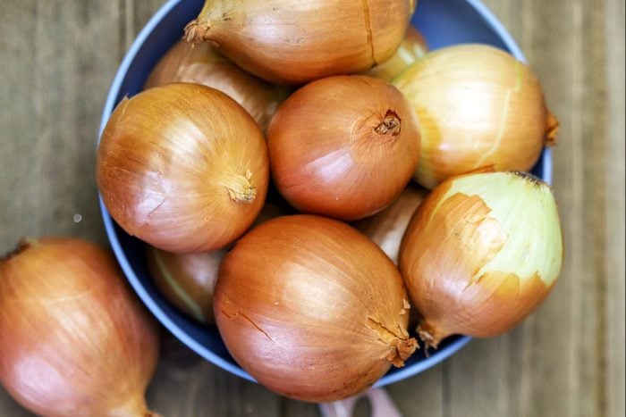 A Group Of Organic Yellow Onions In A Blue Bowl On A Wooden Cutting Board