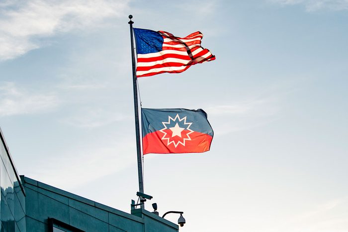 the american flag and the juneteenth flag wave atop a building with the early evening sky background