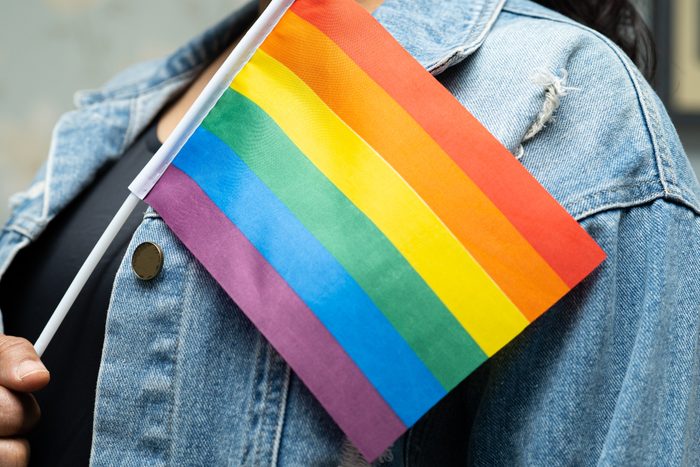 anonymous lgbtq ally wearing denim jacket and holding rainbow pride flag