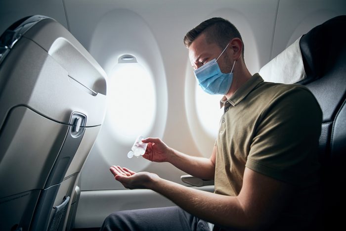 Man wearing face mask and using hand sanitizer inside an airplane