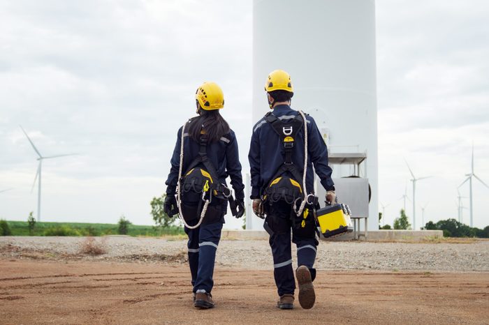 Two Electric engineer wearing Personal protective equipment working in wind turbine farm.