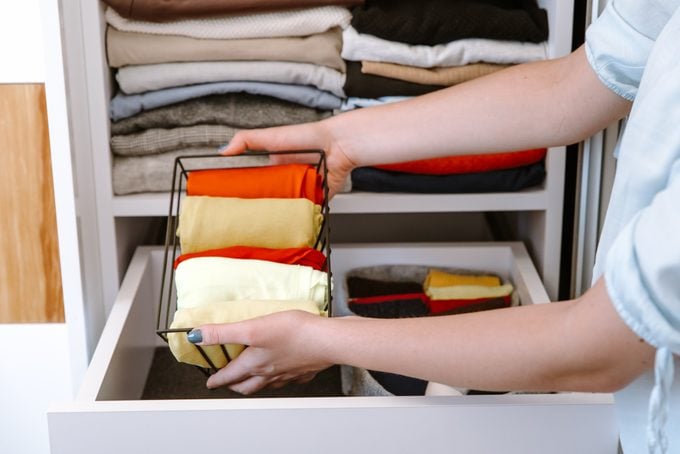 Woman organizing clothes in her closet, putting shirts in boxes and baskets into shelves and drawers.