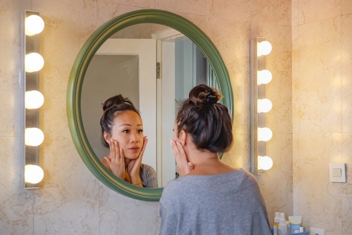Worried East Asian woman checking her face skin in the mirror.