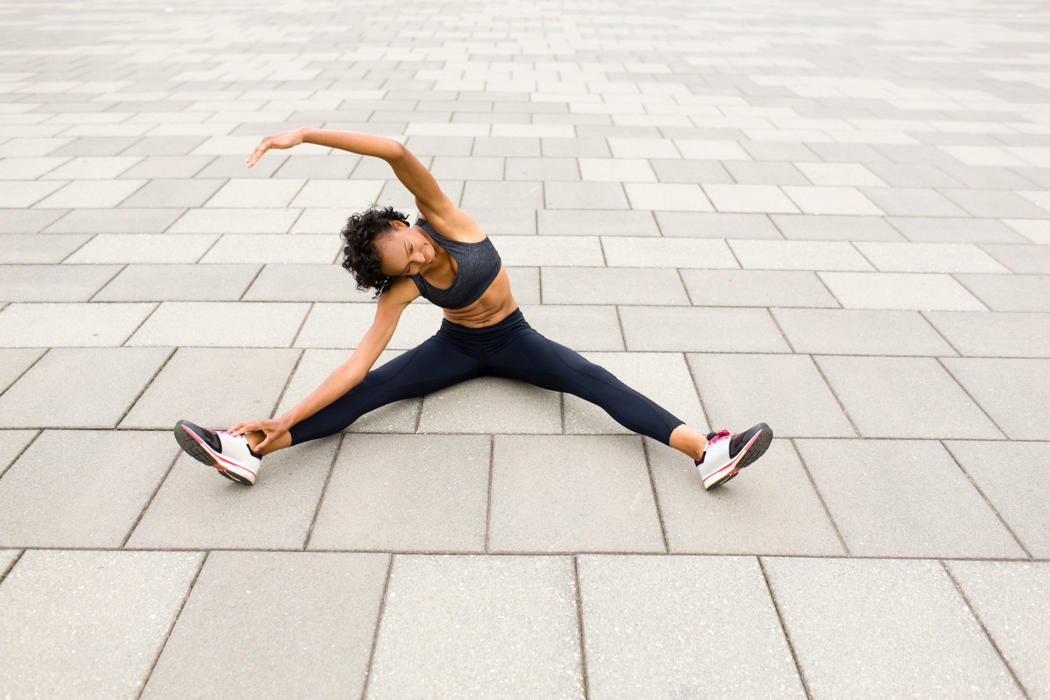 Woman sitting on pavement legs apart doing stretching exercises