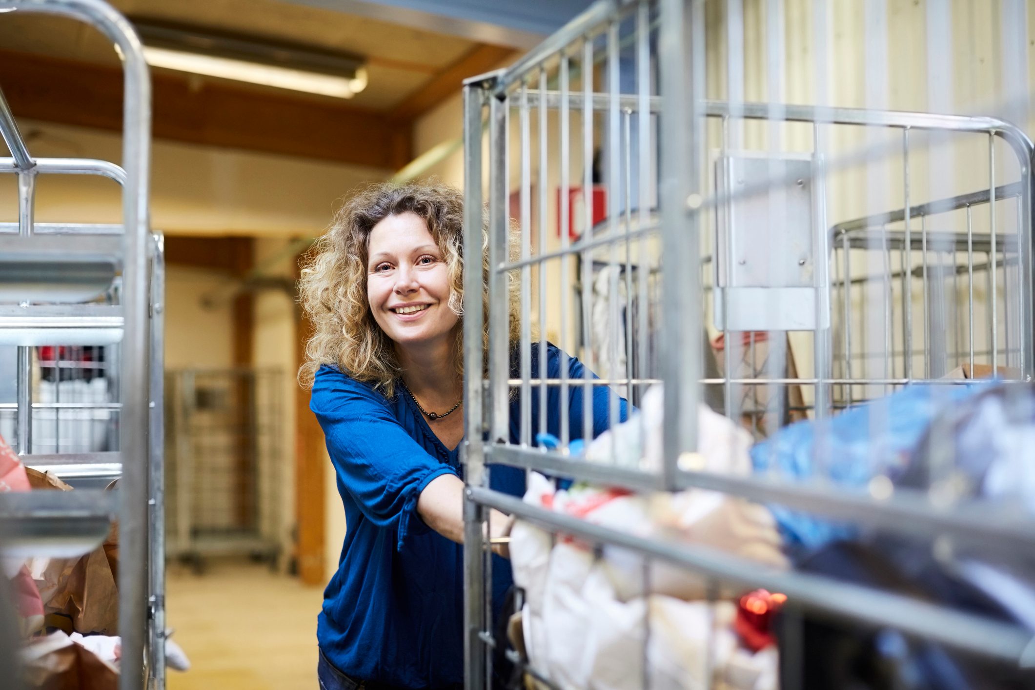 Smiling mature female volunteer pushing cart while looking away at warehouse