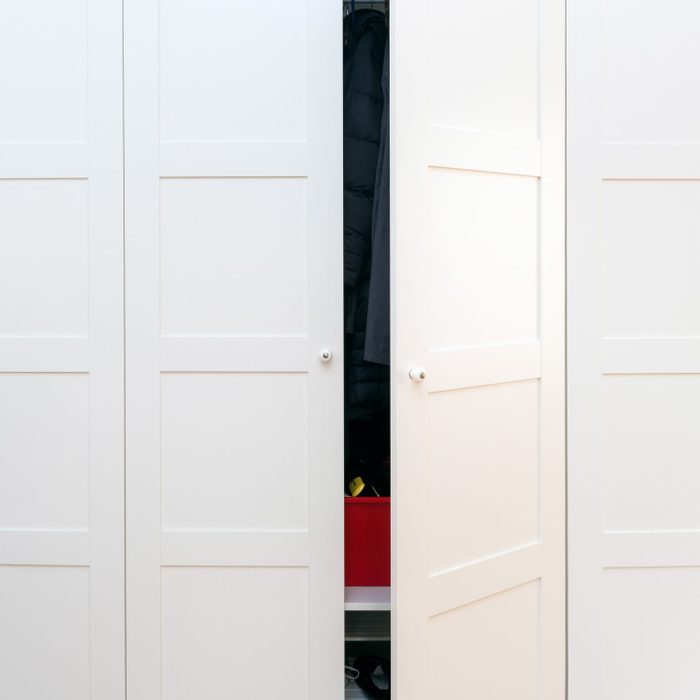 Modern white wooden closet door ajar to show organized interior