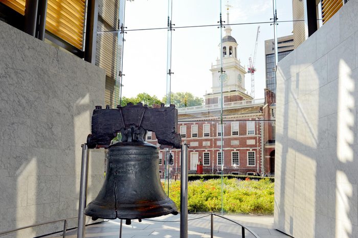 the liberty bell in a museum with the view of Philadelphia out the glass window