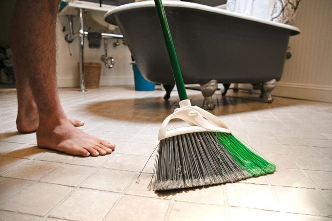 man sweeping bathroom floor before he mops it