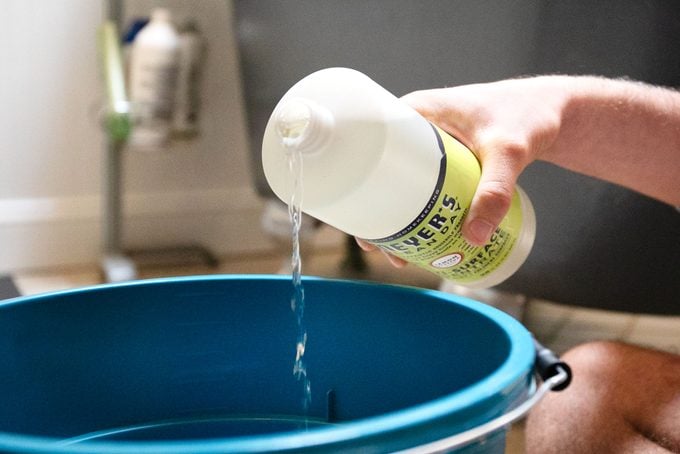 man pouring cleaning agent into bucket to prep for mopping