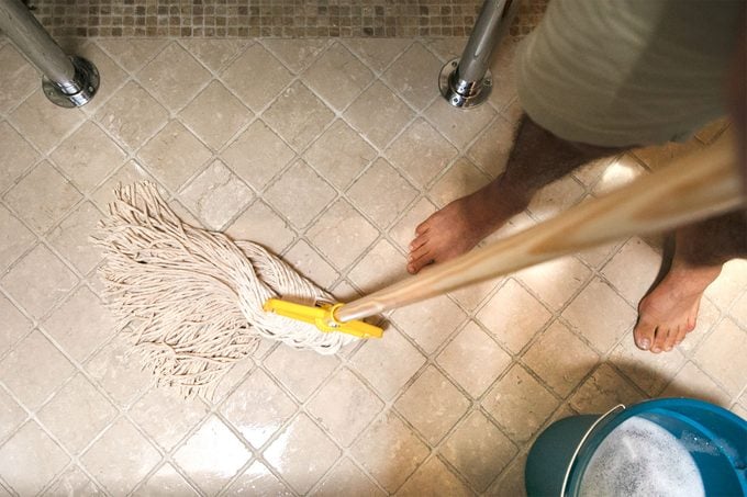 man moping bathroom floor in swishing motion