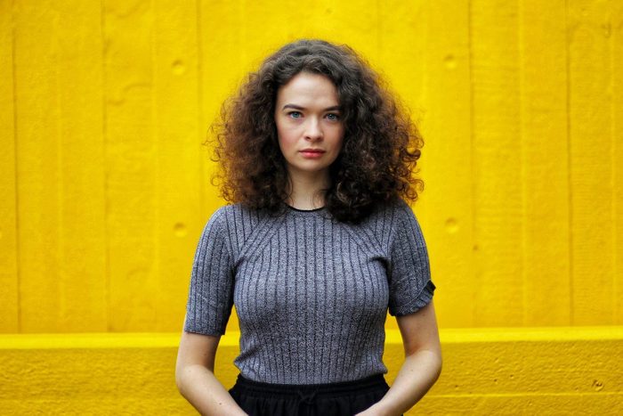 Portrait Of Woman With Curly Hair Standing Against Yellow Wall