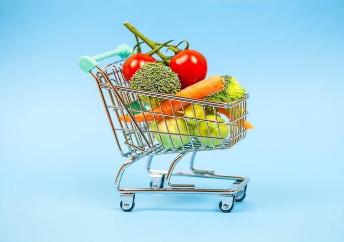 Vegetables in miniature shopping cart on blue background