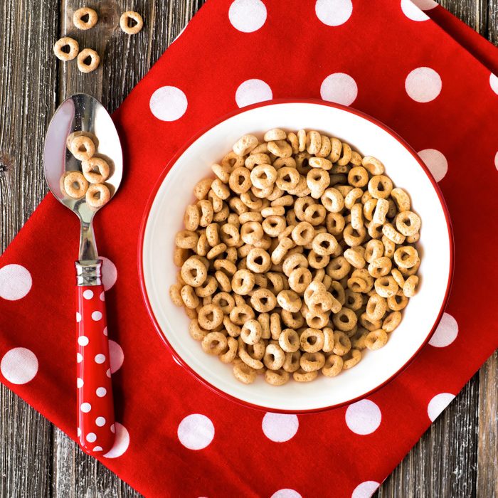 Bowl of cheerios breakfast cereal and polka dot napkin with spoon on wood background