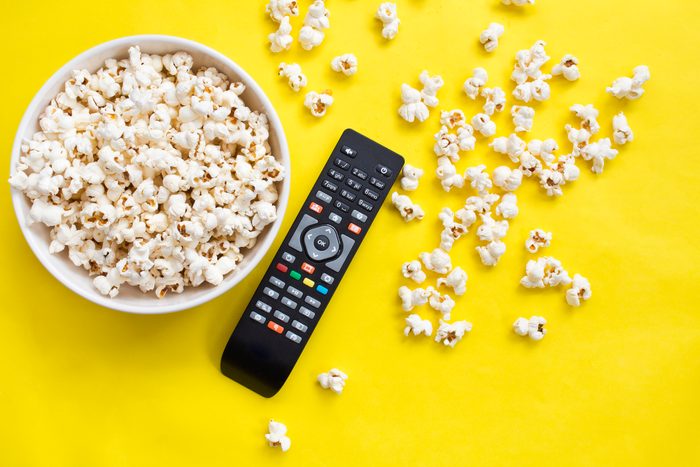 Popcorn and remote control from above on yellow background.