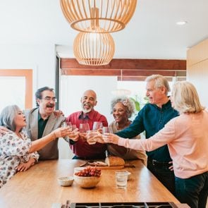 Happy multi-ethnic friends toasting drinks at kitchen island. Retired senior men and women are in kitchen enjoying brunch at home.