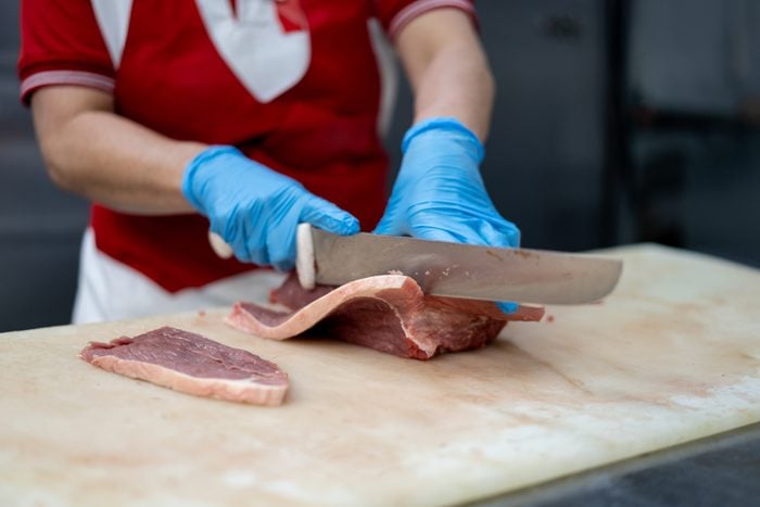 Unrecognizable female butcher cutting a slice of meat