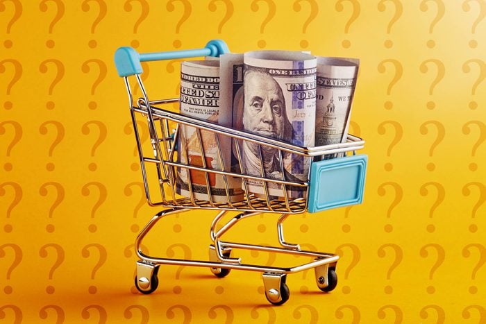 miniature shopping cart with rolled up hundred dollars bills on amazon yellow background with question marks