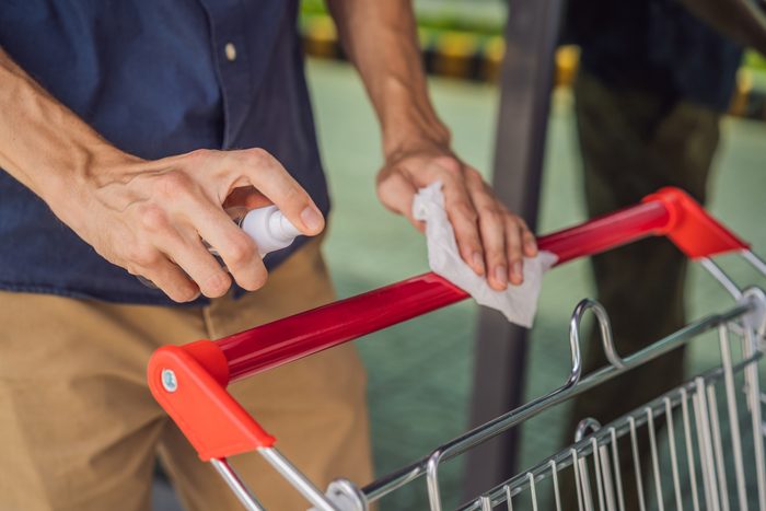 Man's hands disinfecting shopping cart at the grocery store with alcohol spray and wipe
