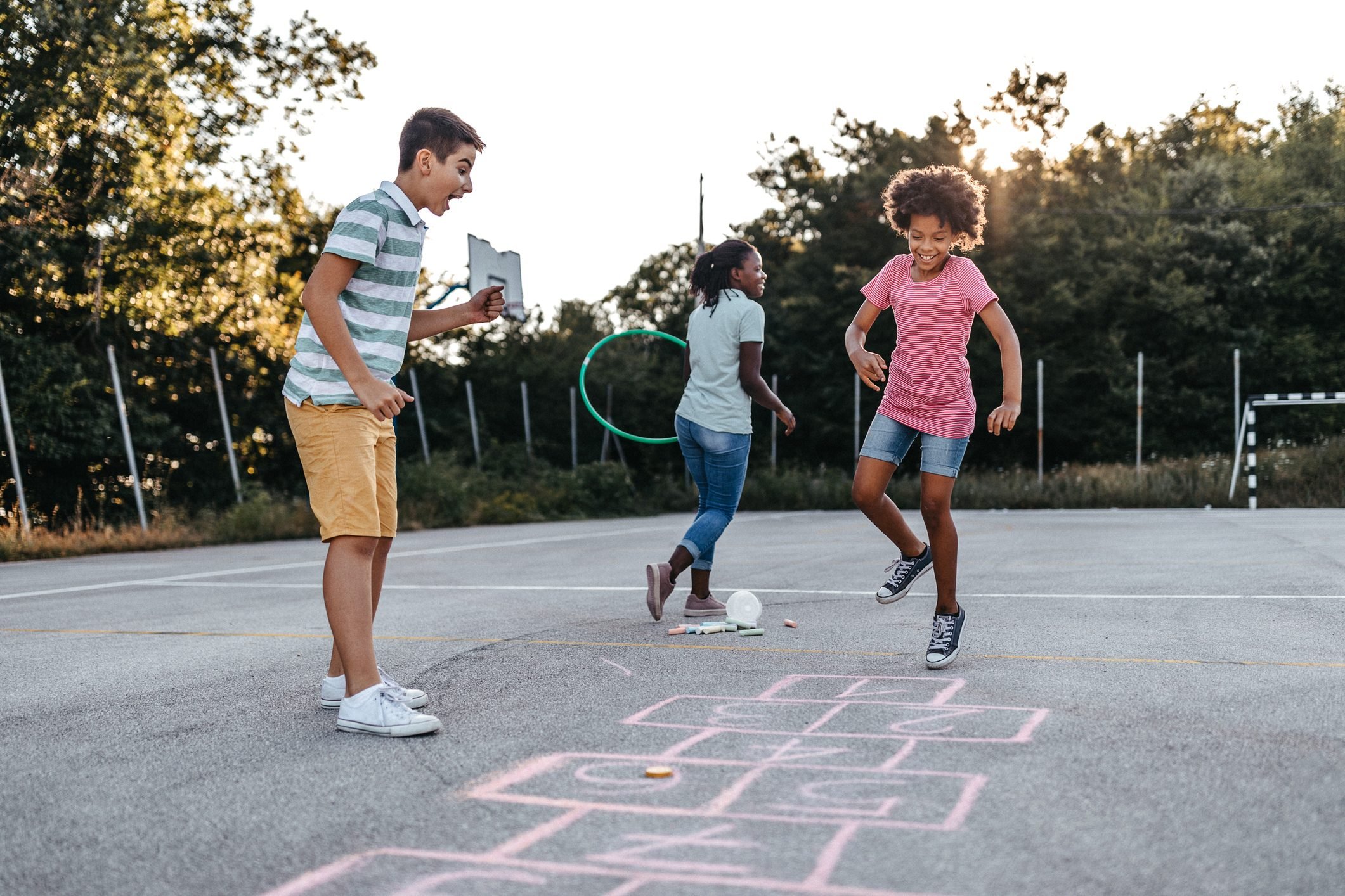 Mother holding plastic hoop while children playing hopscotch