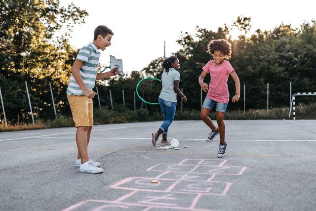 Mother holding plastic hoop while children playing hopscotch