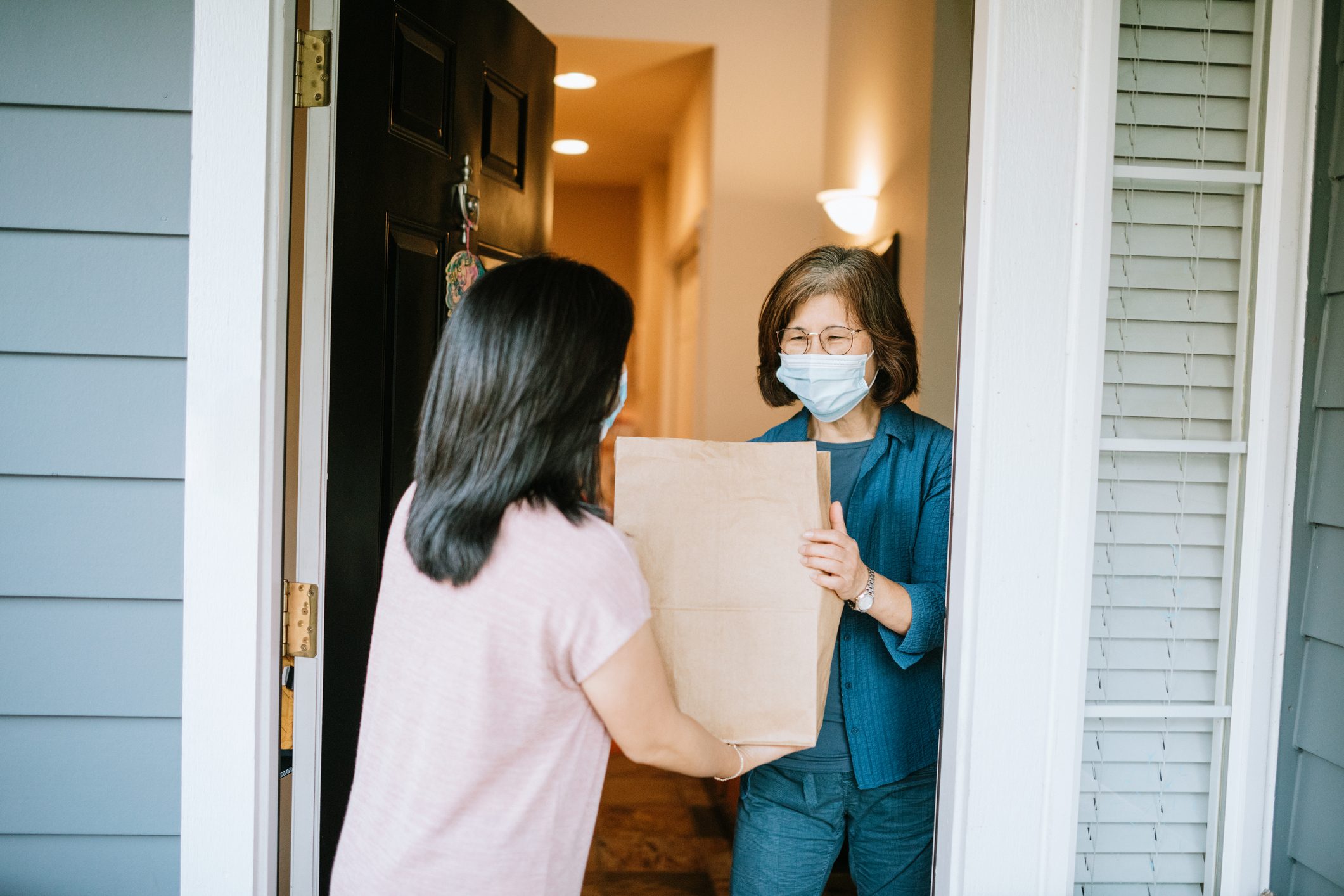Adult Woman Delivers Groceries to older woman wearing a mask