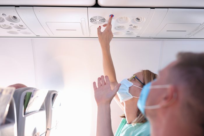 Man and a woman in protective medical masks press call button on plane.