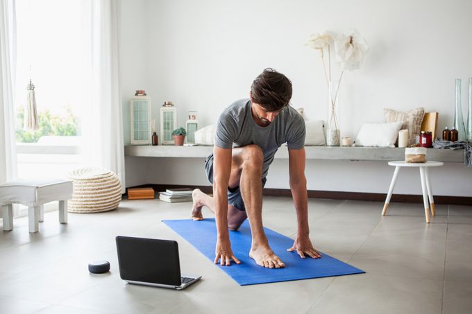 Man doing yoga indoors next to laptop and amazon alexa smart speaker