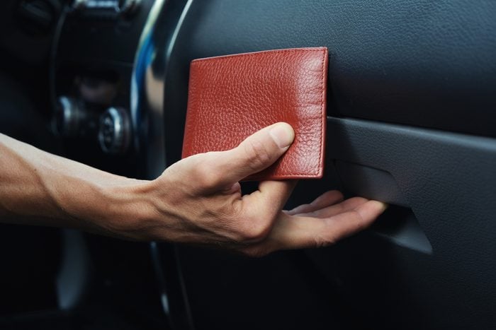 Man hand puts leather wallet in the glove compartment box inside car.