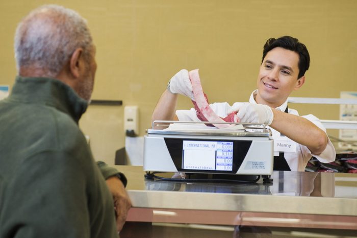 Butcher serving customer meat counter of grocery store
